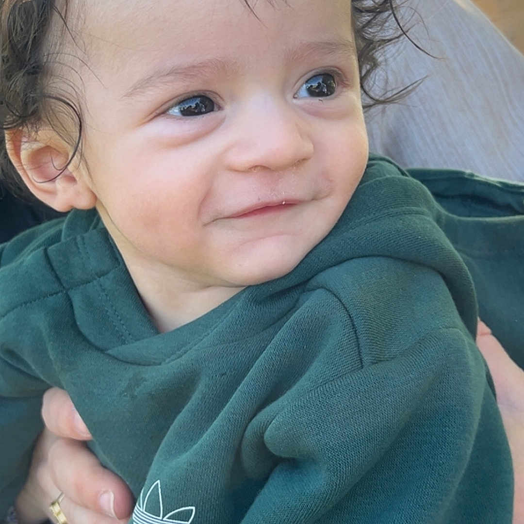 Abdelkader a rejoint le concours — aidez-le/la à gagner de superbes lots ! toddler, child, smile, curly_hair, green_hoodie, outdoor, person, baby, face, portrait, happy, young_child, casual_clothing, holding, daylight, cute, head_and_shoulders, skin, human, apparel