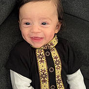 Abdelkader a rejoint le concours — aidez-le/la à gagner de superbes lots ! baby, child, smiling, happy, face, portrait, sitting, clothing, patterned_clothing, long_sleeves, black_clothing, white_sleeves, couch, furniture, indoors, cute, young_child, person, hair, skin