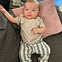 baby, infant, child, couch, pillow, clothing, striped_pants, beige_tshirt, face, barefoot, indoor, floor_tiles, baby_bottle, relaxed, portrait, person, home, cute, skin, furniture