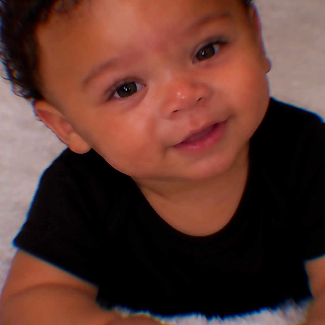 Jayceon is registered to the contest to win money with this photo: baby, child, infant, portrait, smiling, happy, face, curly_hair, black_shirt, white_blanket, indoor, close_up, sitting, hands, eyes, nose, mouth, soft_texture, adorable, photography