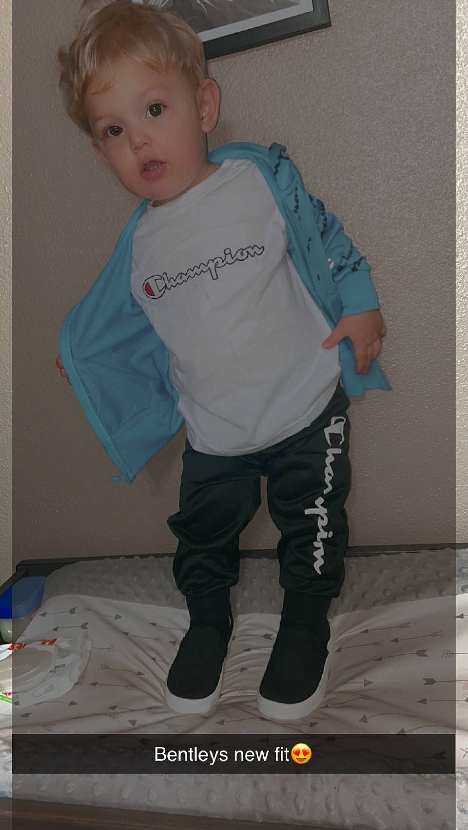 Bentley is registered to the contest to win money with this photo: arm, baby_toddler_clothing, denim, elbow, electric_blue, face, human_leg, jersey, knee, leg, neck, outerwear, person, personal_protective_equipment, sleeve, sportswear, surprise, t_shirt, thigh, toddler