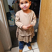 Camila is registered to the contest to win money with this photo: child, girl, braids, indoor, standing, leopard_print, jeans, brown_shoes, beige_top, doorway, carpet, tile_floor, baby_wipes, furniture, expression, cute, person, home, young, casual_clothing