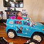 Camila is registered to the contest to win money with this photo: child, toy_car, smiling, indoor, living_room, television, fireplace, wood_floor, girl, red_shirt, play, frozen_theme, decor, happy, seat, window, hair_tied, footwear, pajamas, furniture