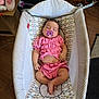 baby, baby_care, baby_lounger, cardboard_box, child, cute, floor, household_items, indoor, infant, pacifier, pacifier_clip, patterned_fabric, pink_clothing, relaxing, resting, sleeping, small_person, toddler, wooden_floor