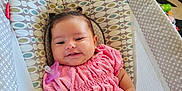 Xiomara is registered to the contest to win money with this photo: baby, baby_seat, carpet, child, cute, furniture, happy, home, indoor, infant, living_room, pacifier, patterned_fabric, person, pigtails, pink_clothing, small_hand, smiling, toy, wood_floor