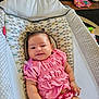 baby, baby_seat, carpet, child, cute, furniture, happy, home, indoor, infant, living_room, pacifier, patterned_fabric, person, pigtails, pink_clothing, small_hand, smiling, toy, wood_floor