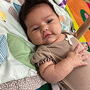 Xiomara joined the competition — help win amazing prizes! baby, blanket, child, clothing, colorful, comfort, cute, face, hand, happy, indoors, infant, lying_down, pattern, portrait, quilt, skin, smile, toddler, young