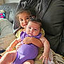 baby, blanket, child, clothing, couch, cozy, cute, face, family, golden_dress, home, hug, indoor, infant, natural_light, person, purple_onesie, sibling, smile, toddler