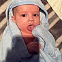 baby, child, towel, blue, hooded_towel, tongue_out, blanket, striped, cute, infant, skin, face, hand, lying_down, soft_texture, cozy, indoors, expression, playful, wrapped