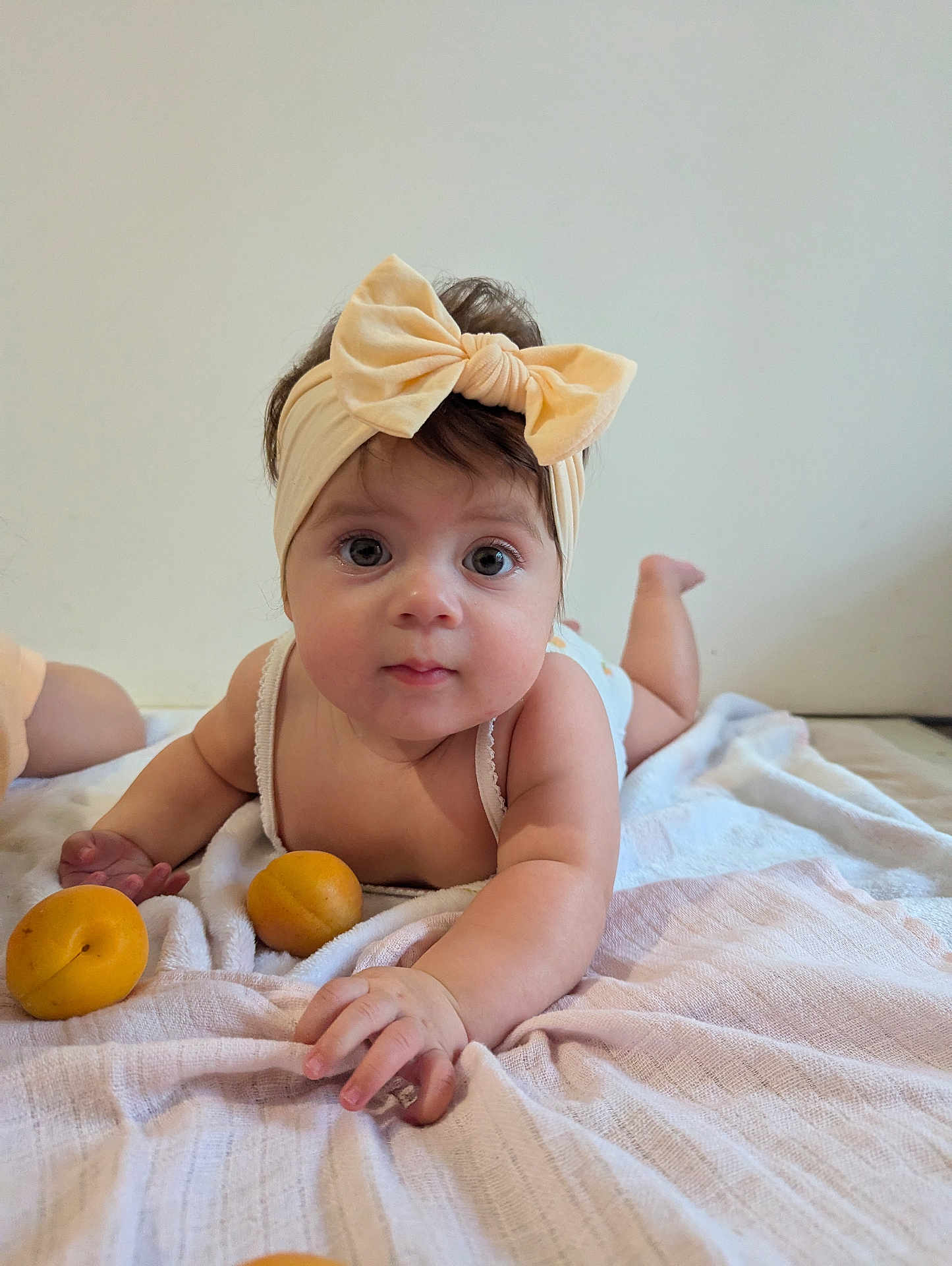 Nëyla participe au concours pour gagner de l'argent avec cette photo : baby, infant, headband, bow, blanket, fruit, apricot, child, cute, lying_down, indoors, soft_lighting, skin, face, hand, eyes, expression, white_background, clothing, toddler