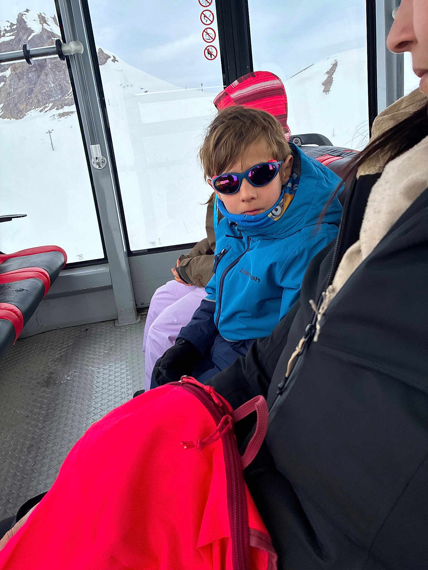 Enzo a rejoint le concours — aidez-le/la à gagner de superbes lots ! child, kid, sunglasses, blue_jacket, scarf, gloves, backpack, snow, mountains, gondola, cabin, window, seat, adult, winter_clothing, portrait, travel, reflection, ski_trip, pink_bag