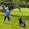 woman, dog, german_shepherd, grass, tree, throwing, playing, outdoor, park, pet, animal, person, leisure, summer, greenery, active, fun, daytime, casual_clothing, nature
