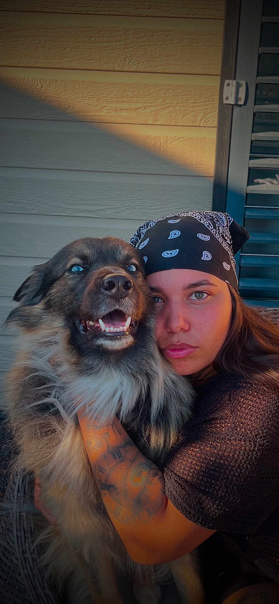 Mowgli participe au concours pour gagner de l'argent avec cette photo : dog, person, tattoo, bandana, outdoor, sunlight, closeup, pet, companion, fur, face, cuddling, portrait, expression, animal, human, warm_light, wall, texture, love