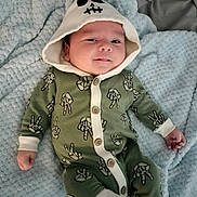 Braxton is registered to the contest to win money with this photo: baby, infant, onesie, hood, skull, peace_sign, skeleton_hand, smiling, blanket, soft_texture, cute, child, lying_down, baby_clothing, portrait, happy, indoors, sock, buttoned, face