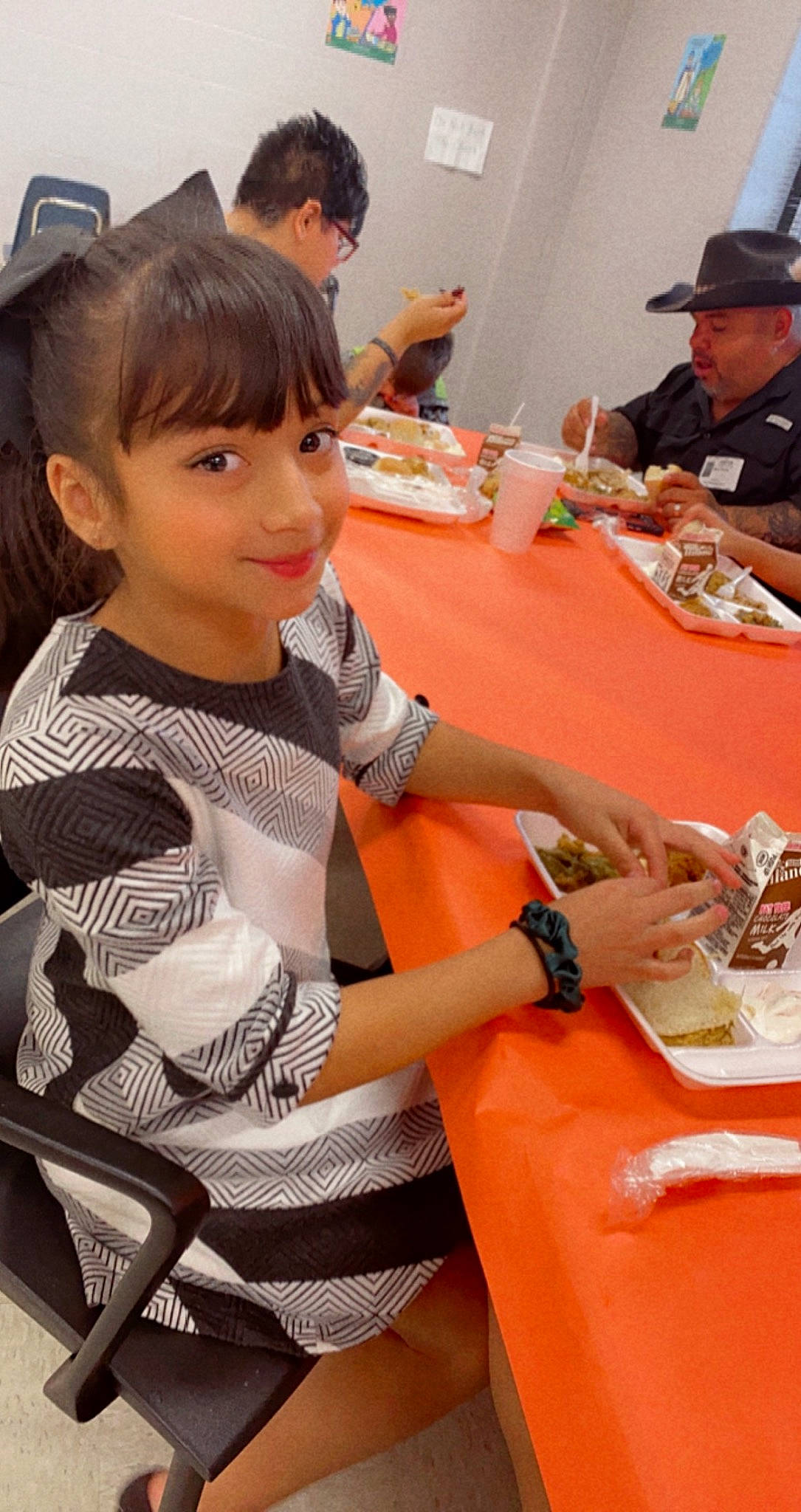 Caylee is registered to the contest to win money with this photo: bangs, chair, child, cuisine, drink, event, food, fun, hat, headwear, joy, leisure, orange, person, plate, recreation, room, sitting, smile, sun_hat