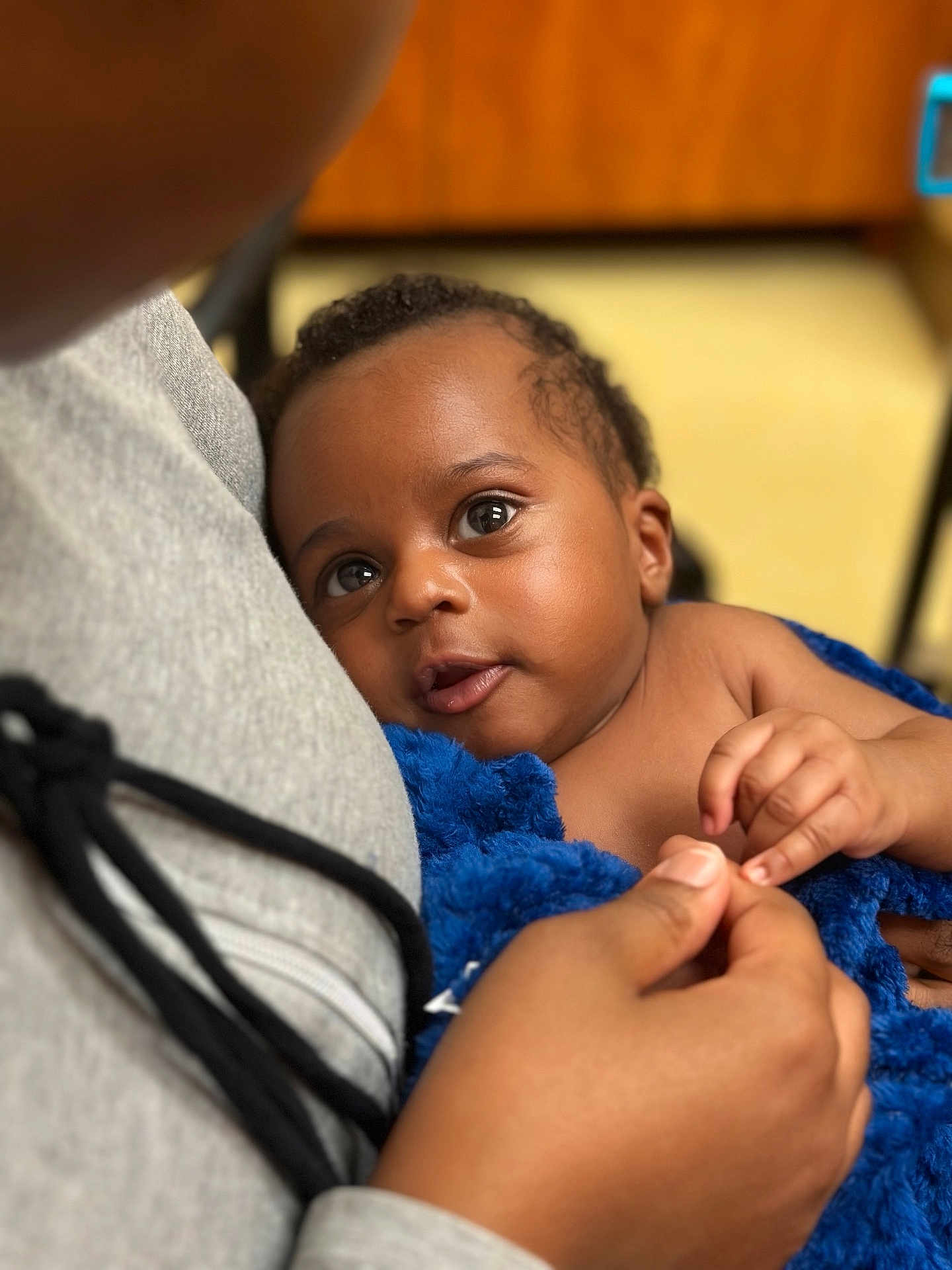Jeremiah joined the competition — help win amazing prizes! baby, child, infant, blue_blanket, holding_hands, close_up, indoor, person, face, curious, soft_texture, gray_hoodie, skin, portrait, young_child, tender_moment, caring, expression, comfort, warmth