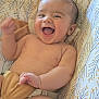 baby, bare_chest, cheerful, child, closeup, cushion, cute, expression, face, happy, indoors, infant, joy, lying_down, patterned_background, person, skin, small_hand, smiling, young