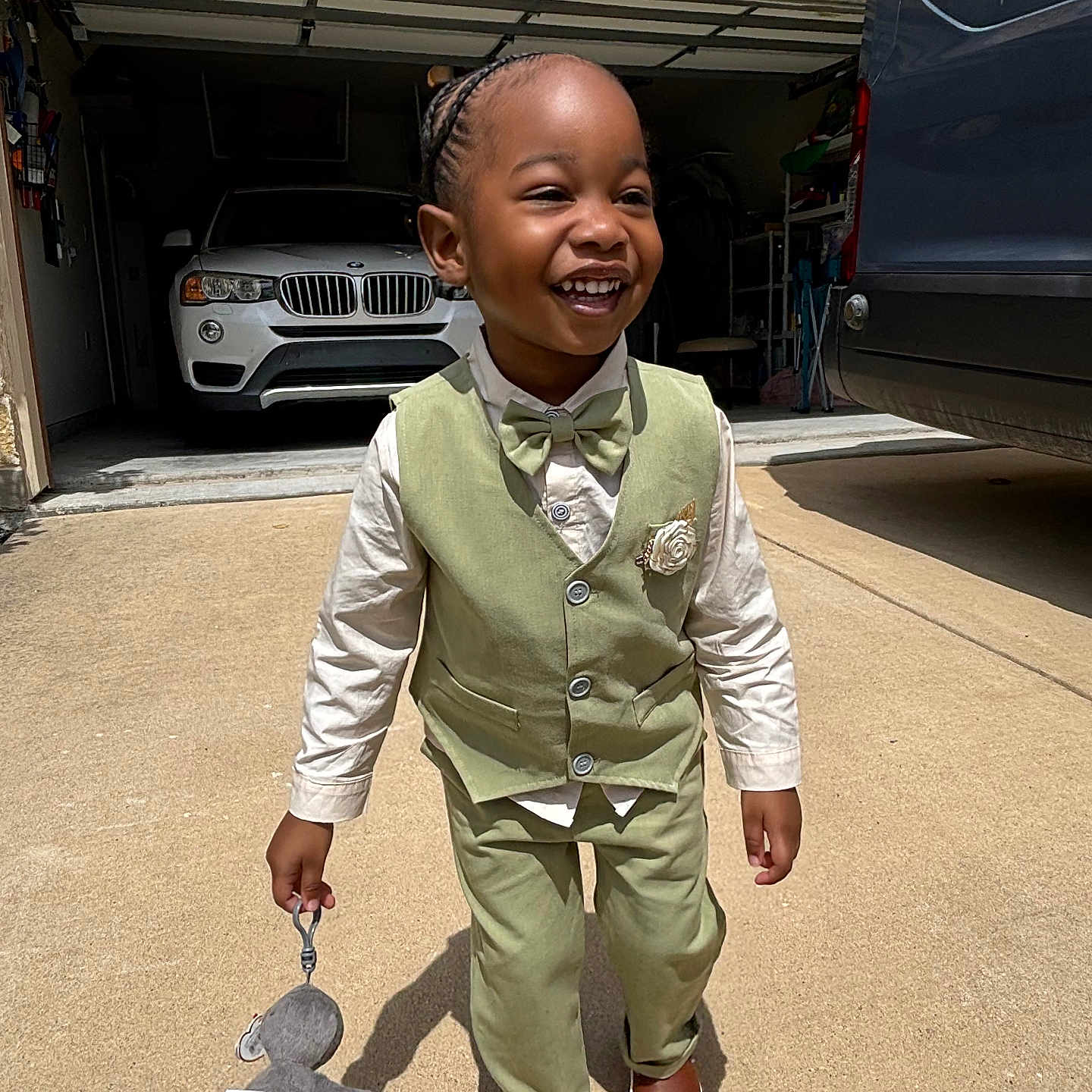 Kamari is registered to the contest to win money with this photo: child, boy, smiling, vest, bow_tie, pants, toy, stuffed_animal, driveway, car, garage, sunlight, shadow, footwear, happy, outdoor, clothing, person, portrait, fashion