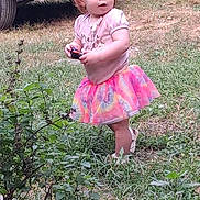 Eden is registered to the contest to win money with this photo: toddler, child, grass, outdoor, toy, car, vehicle, shirt, skirt, footwear, nature, greenery, plants, curly_hair, daylight, backyard, standing, casual_clothing, expression, play