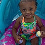 toddler, child, pool, inflatable_float, water, toy, cupcake_toy, curly_hair, pigtails, colorful_swimsuit, summer, outdoor, playful, smiling, sitting, fun, swimming_pool, baby, cute, portrait