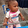 aisle, baby, baby_clothing, cart, child, clothing_store, cookie_pattern, curious, face, indoor, pink_outfit, portrait, retail, serious_expression, shopping, shopping_cart, sitting, store, toddler, walmart
