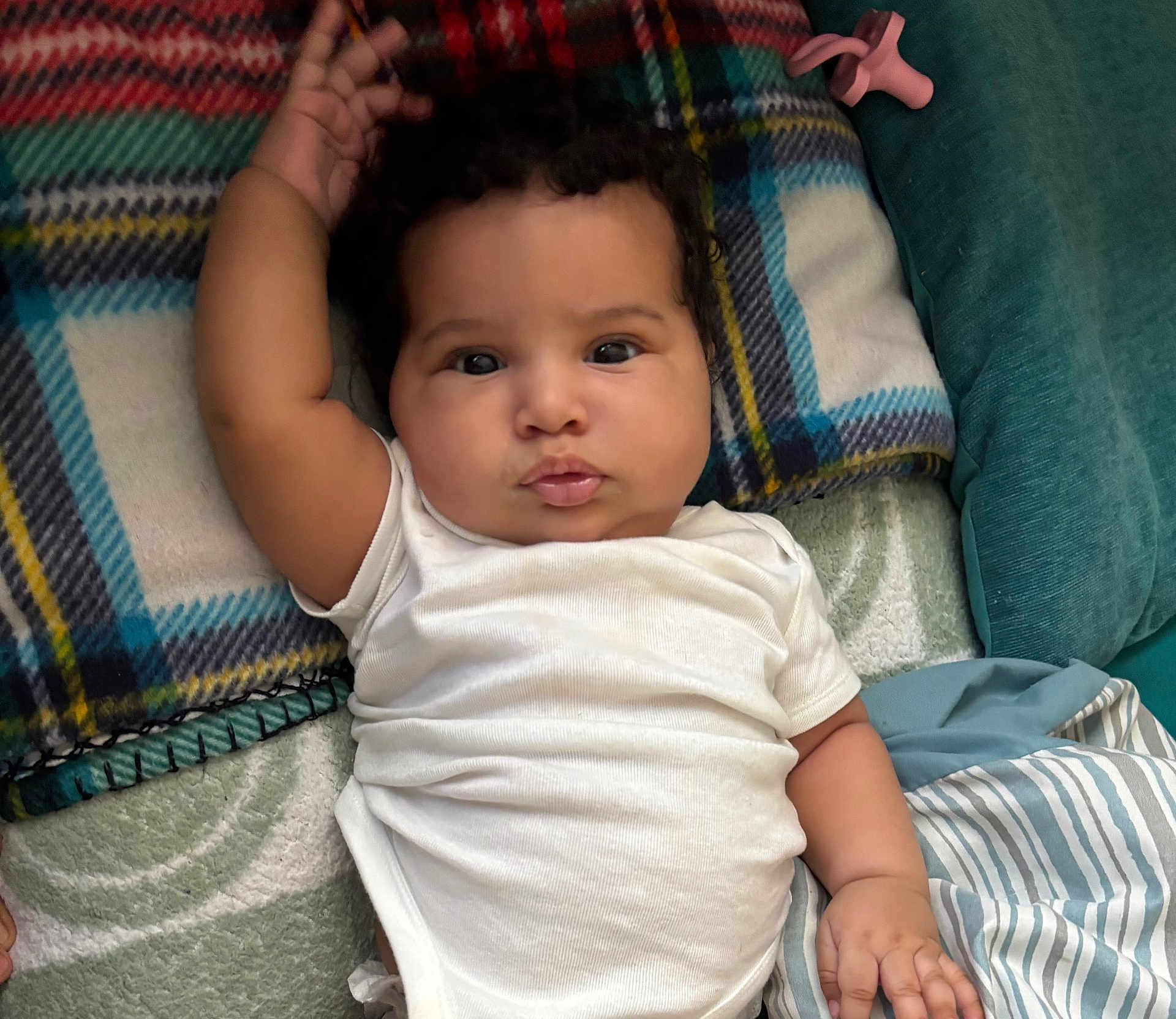 Kahlani Forman is registered to the contest to win money with this photo: baby, child, infant, white_onesie, blanket, cushion, plaid, striped, hand, face, curly_hair, lying_down, indoors, soft_texture, cute, portrait, skin, expression, comfort, resting