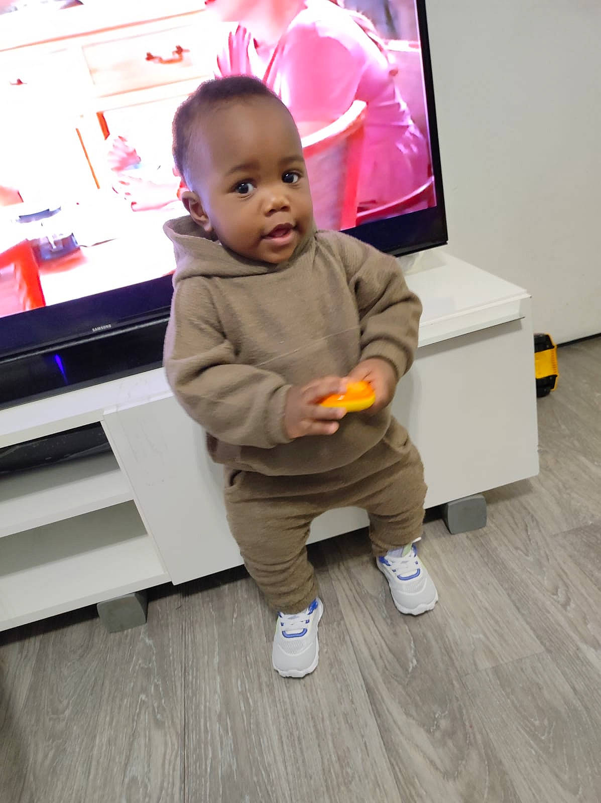 Eliel participe au concours pour gagner de l'argent avec cette photo : baby, baby_toddler_clothing, child, display_device, face, floor, flooring, fun, gadget, hardwood, home_appliance, laminate_flooring, person, room, shoe, sneakers, t_shirt, television_set, toddler, wood
