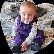 Leland is registered to the contest to win money with this photo: baby, child, purple_vest, bowtie, sitting, blanket, indoor, cute, portrait, infant, face, eyes, smile, clothing, footwear, hands, cozy, soft_texture, heart_frame, curious
