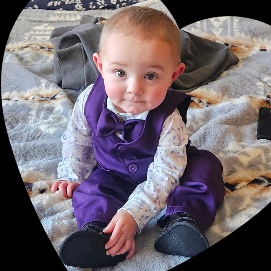 Leland is registered to the contest to win money with this photo: baby, child, purple_vest, bowtie, sitting, blanket, indoor, cute, portrait, infant, face, eyes, smile, clothing, footwear, hands, cozy, soft_texture, heart_frame, curious
