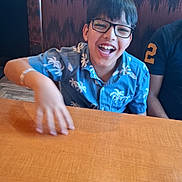 Kumar Laksh is registered to the contest to win money with this photo: child, boy, glasses, smiling, blue_shirt, tropical_pattern, table, restaurant, booth, indoor, happy, person, seated, wood, furniture, casual, laughter, hair, face, clothing