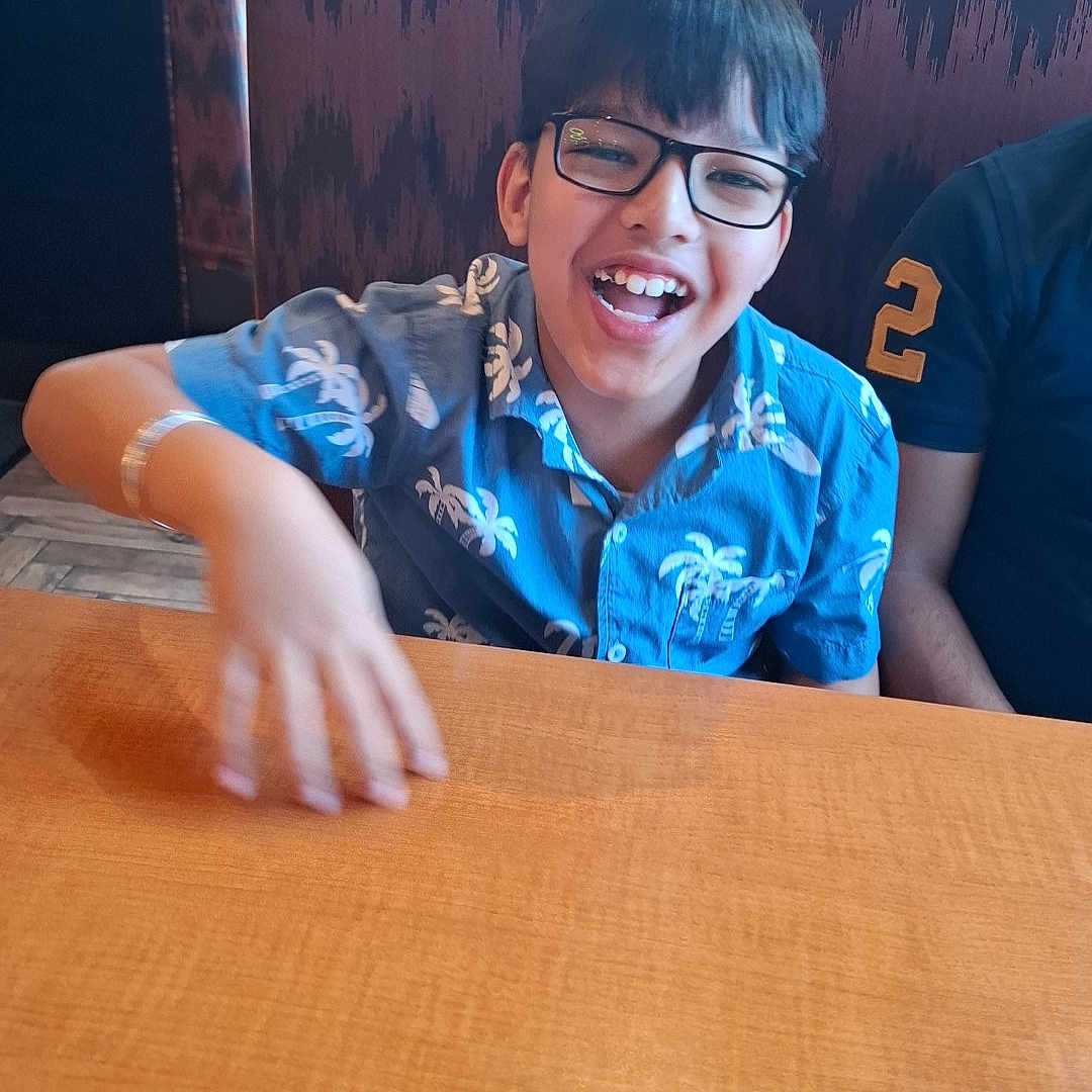 Kumar Laksh is registered to the contest to win money with this photo: blue_shirt, booth, boy, casual, child, clothing, face, furniture, glasses, hair, happy, indoor, laughter, person, restaurant, seated, smiling, table, tropical_pattern, wood