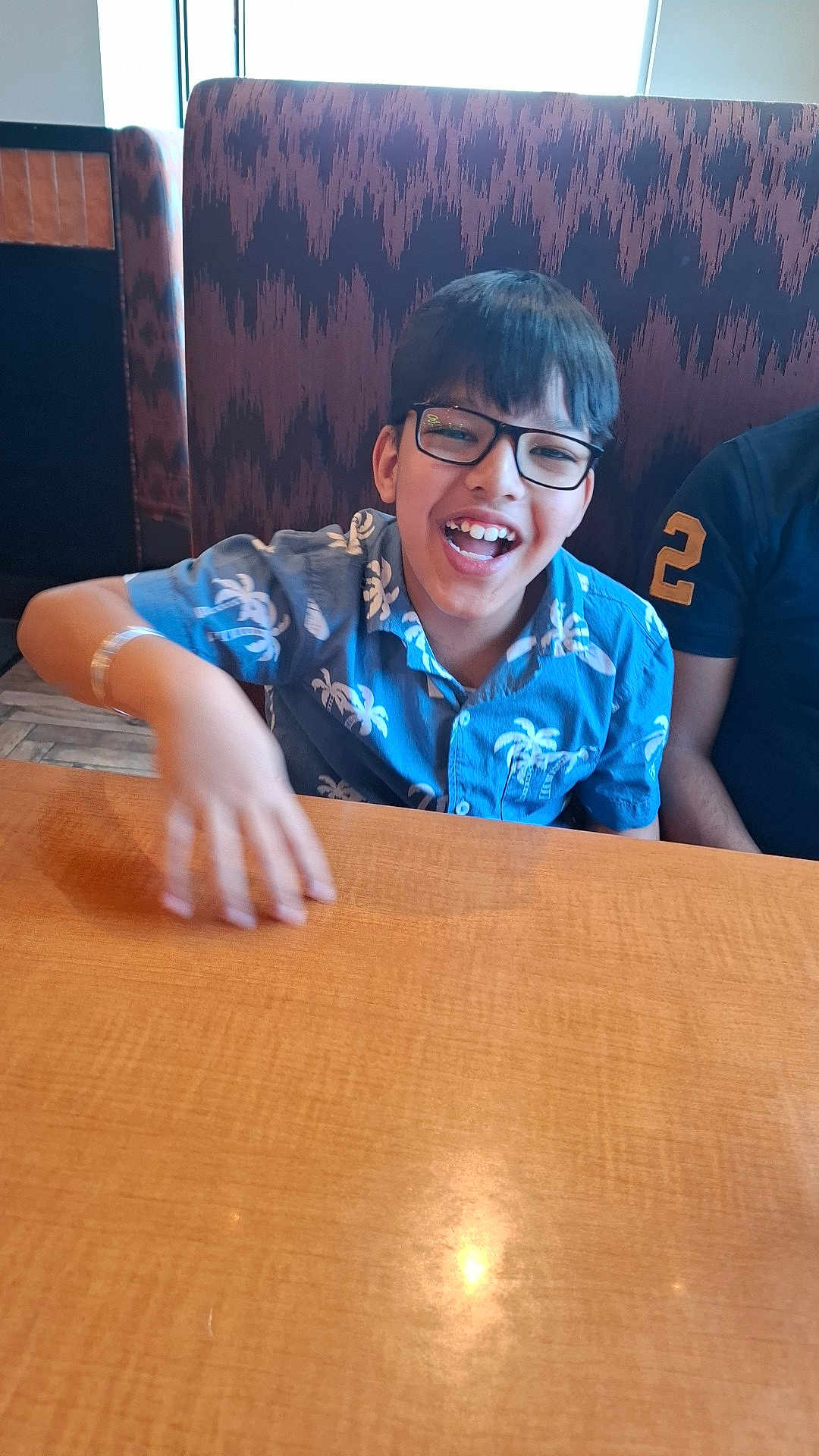 Kumar Laksh is registered to the contest to win money with this photo: child, boy, glasses, smiling, blue_shirt, tropical_pattern, table, restaurant, booth, indoor, happy, person, seated, wood, furniture, casual, laughter, hair, face, clothing