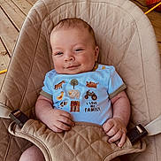 Huddson is registered to the contest to win money with this photo: baby, smile, baby_seat, quilted, blue_shirt, farm_animals, text_on_clothing, wooden_deck, pumpkin, hand, face, infant, cute, happy, indoor, comfort, clothing, person, portrait, relaxation