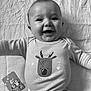 baby, infant, smiling, onesie, reindeer_graphic, milestone_card, blanket, lying_down, cute, happy, child, clothing, face, portrait, arm, indoors, young, person, baby_girl, baby_boy