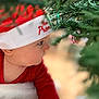 baby, candid, celebration, child, christmas_hat, christmas_tree, curious, cute, face, festive, greenery, holiday, indoors, infant, pine_needles, portrait, profile, red_clothing, seasonal, soft_focus