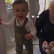 Kinay a rejoint le concours — aidez-le/la à gagner de superbes lots ! toddler, child, smiling, window, overalls, necklace, indoor, adult, doll, holding, standing, footwear, white_socks, window_frame, daylight, happy, person, baby_doll, clothing, home