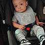 baby, child, car_seat, bib, striped_pants, sneakers, indoor, seated, curious_expression, clothing, footwear, person, young_child, cute, infant, safety_buckle, head, face, hands, legs