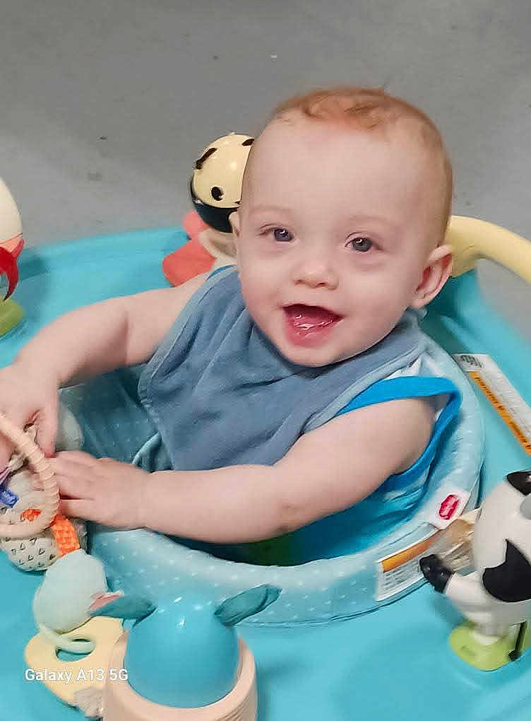 Mason joined the competition — help win amazing prizes! baby, child, smiling, blue_bib, baby_activity_center, toy, indoor, happy, infant, playtime, cute, face, person, seat, plastic_toy, colorful, young_child, cheerful, baby_toys, early_childhood