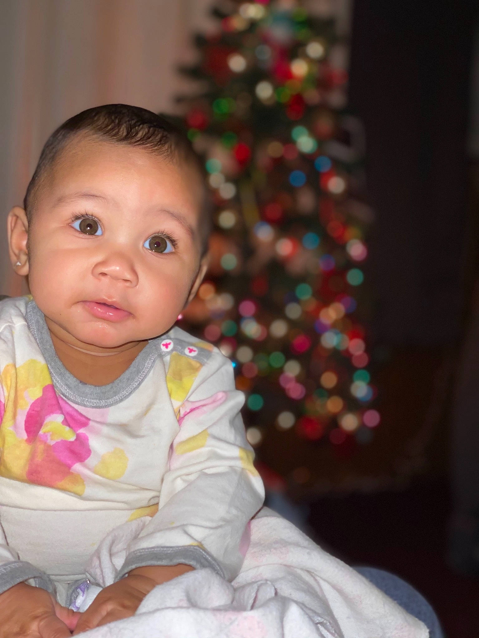 Persia is registered to the contest to win money with this photo: baby, baby_toddler_clothing, cheek, child, christmas_decoration, christmas_eve, christmas_ornament, christmas_tree, conifer, event, eye, fun, happy, head, holiday, holiday_ornament, person, sitting, sleeve, toddler