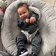 Memphis is registered to the contest to win money with this photo: baby, baby_chair, black_shoes, blanket, child, clothing, cute, diapers, dimples, floor_tiles, gray_outfit, happy, home_decor, indoor, infant, nike_sneakers, person, plush, seated, smiling