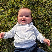 Romy a rejoint le concours — aidez-le/la à gagner de superbes lots ! baby, infant, child, smile, grass, outdoor, lying_down, cheeks, hands, white_shirt, navy_pants, portrait, happy, nature, sunlight, ground, casual_clothing, playful, cute, weekend