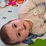 baby, infant, lying_down, play_mat, toy, rattle, teething_necklace, smile, eyes, face, onesie, clothing, playtime, indoor, closeup, portrait, colorful, happy, child, nursery