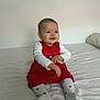 baby, child, smiling, red_dress, white_shirt, white_tights, heart_pattern, bed, pillow, indoor, cute, sitting, happy, young_child, portrait, infant, person, human, cozy, casual