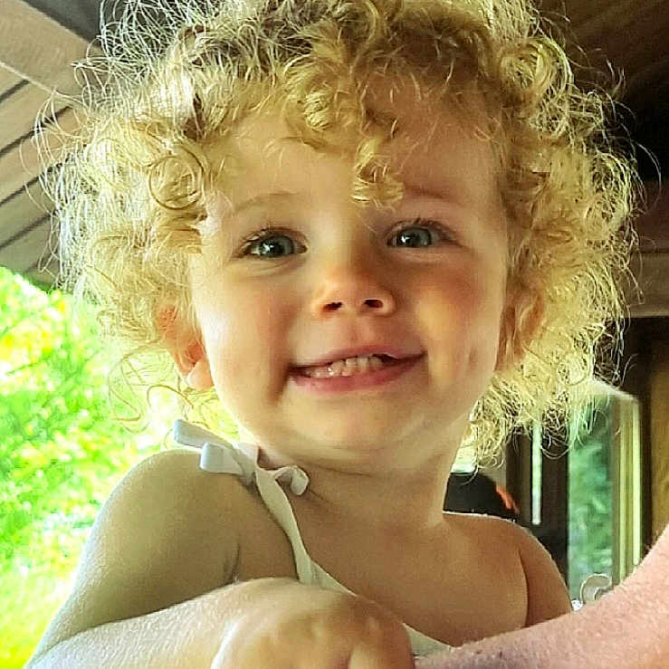 Angel Agathe a rejoint le concours — aidez-le/la à gagner de superbes lots ! baby_clothes, bright, child, close_up, curly_hair, cute, dimples, face, greenery, hand, happy, holding, indoor, natural_light, person, portrait, skin, smile, toddler, wooden_ceiling