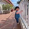 toddler, child, outdoor, terrace, railing, plants, potted_plants, sunny, daylight, blue_sky, curious, clothing, denim_vest, jeans, shoes, tiles, shadow, building, handrail, person