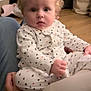 baby, blonde_hair, child, clothing, cozy, curly_hair, cute, expression, eyes, face, floor, hand, indoor, infant, lap, onesie, person, sitting, stars_pattern, wooden_floor