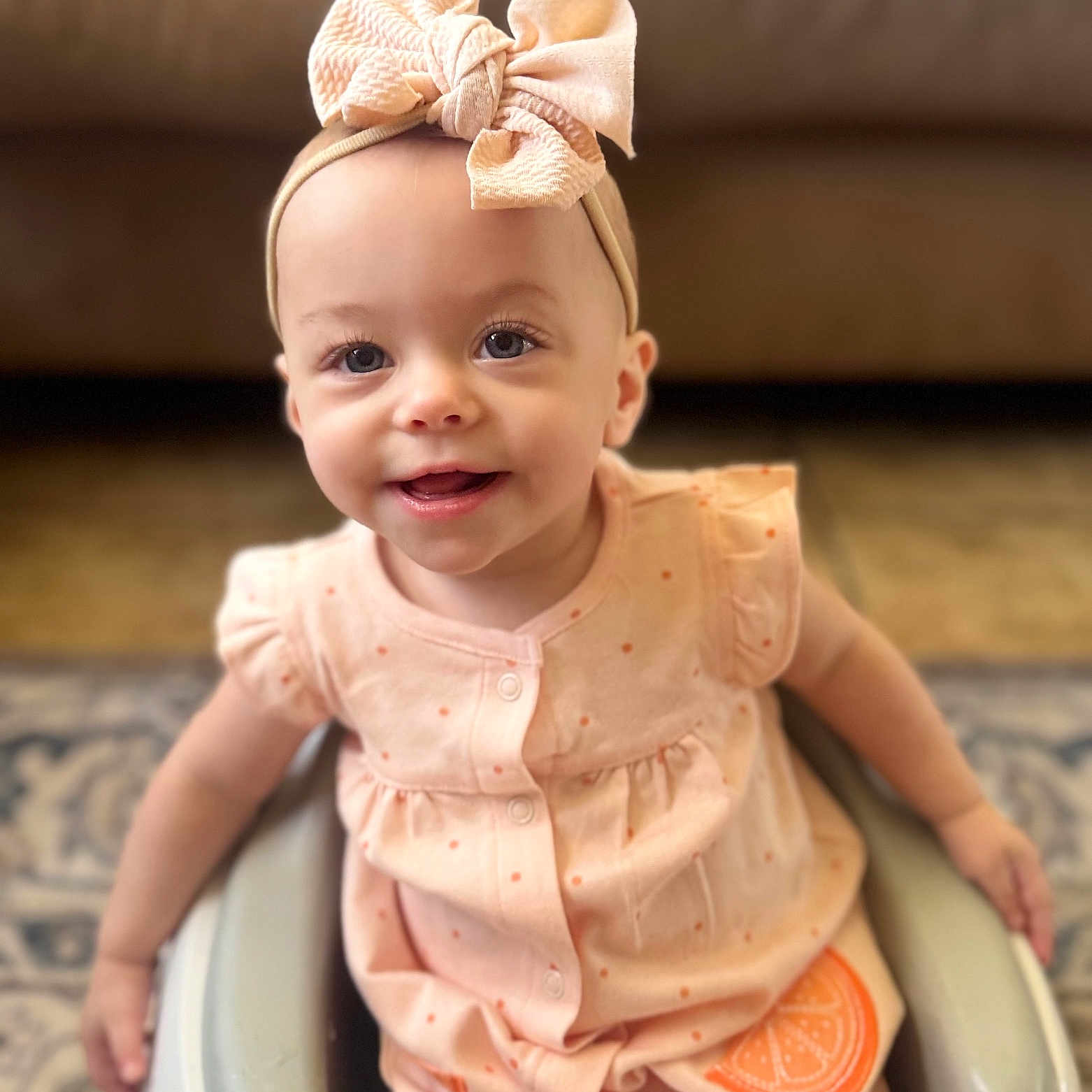 Emberley is registered to the contest to win money with this photo: baby, bow, carpet, child, clothing, cute, furniture, happy, headband, indoor, infant, orange_slice, peach, person, portrait, seat, sitting, smile, toddler, young