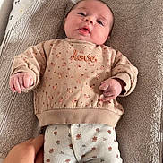 Rose participe au concours pour gagner de l'argent avec cette photo : baby, bedroom, cartoon_print, changing_pad, child, clothing, cute, expression, face, floral_pattern, hand, indoor, infant, lying_down, mickey_mouse, pants, person, soft_fabric, sweater, towel