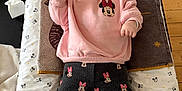 Rose participe au concours pour gagner de l'argent avec cette photo : baby, changing_pad, child, clothing, cute, expression, face, floor, indoor, infant, lying_down, mickey_mouse, minnie_mouse, patterned_pants, person, pink_sweatshirt, soft_toys, towel, white_socks, wooden_table