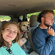 Mocha is registered to the contest to win money with this photo: woman, dog, man, car, seat, seatbelt, tattoo, driving, road_trip, smile, casual, indoors, daylight, window, nature, greenery, pet, leash, portrait, travel
